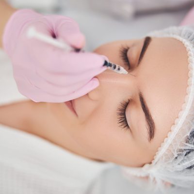 Beautician hand introducing a syringe between woman eyebrows for face skin enhancement